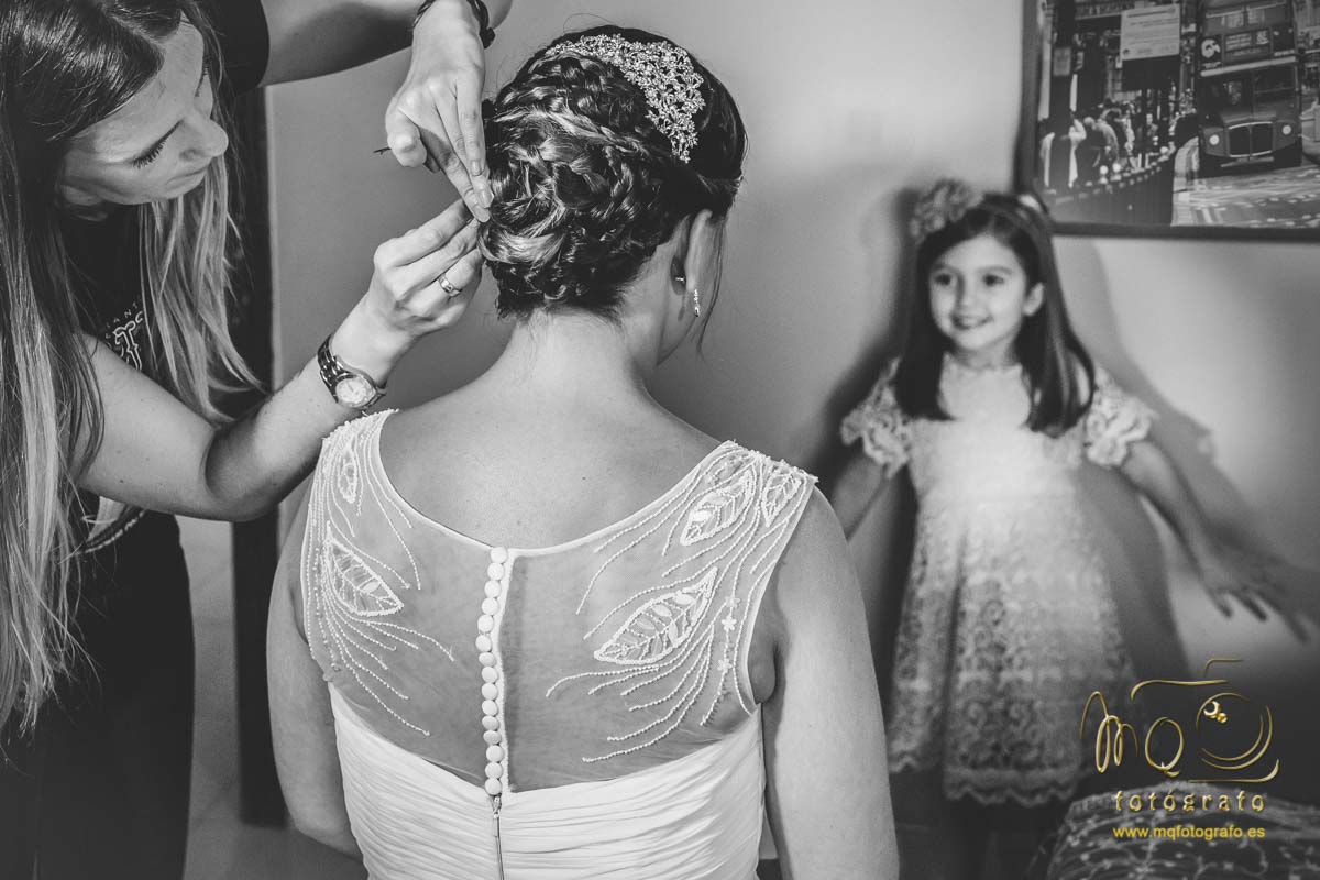 peluquera arreglando el moño de la novia y niña mirándola